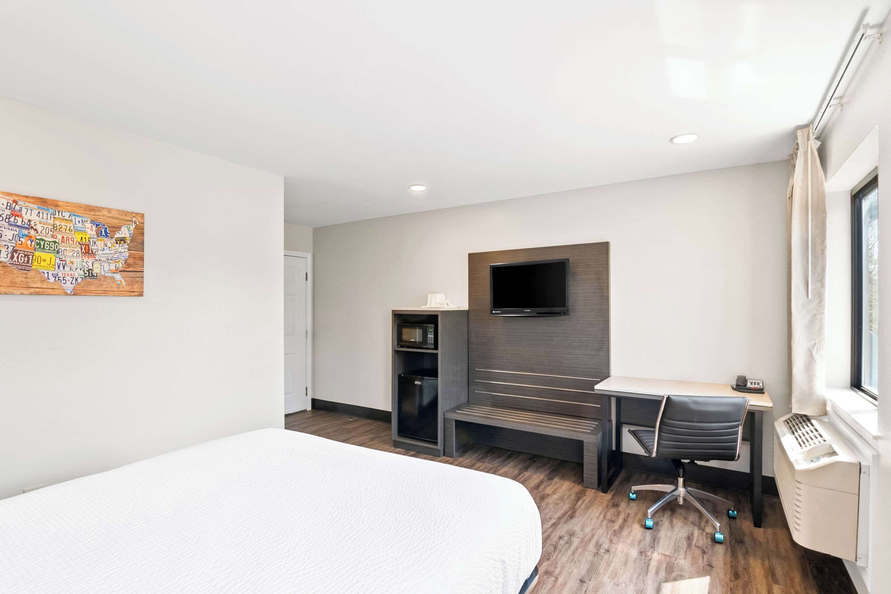 A modern hotel room with a bed, a desk with a chair, a flat-screen TV mounted on the wall, a microwave, and a heater.