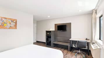 A modern hotel room with a bed, a desk with a chair, a flat-screen TV mounted on the wall, a microwave, and a heater.
