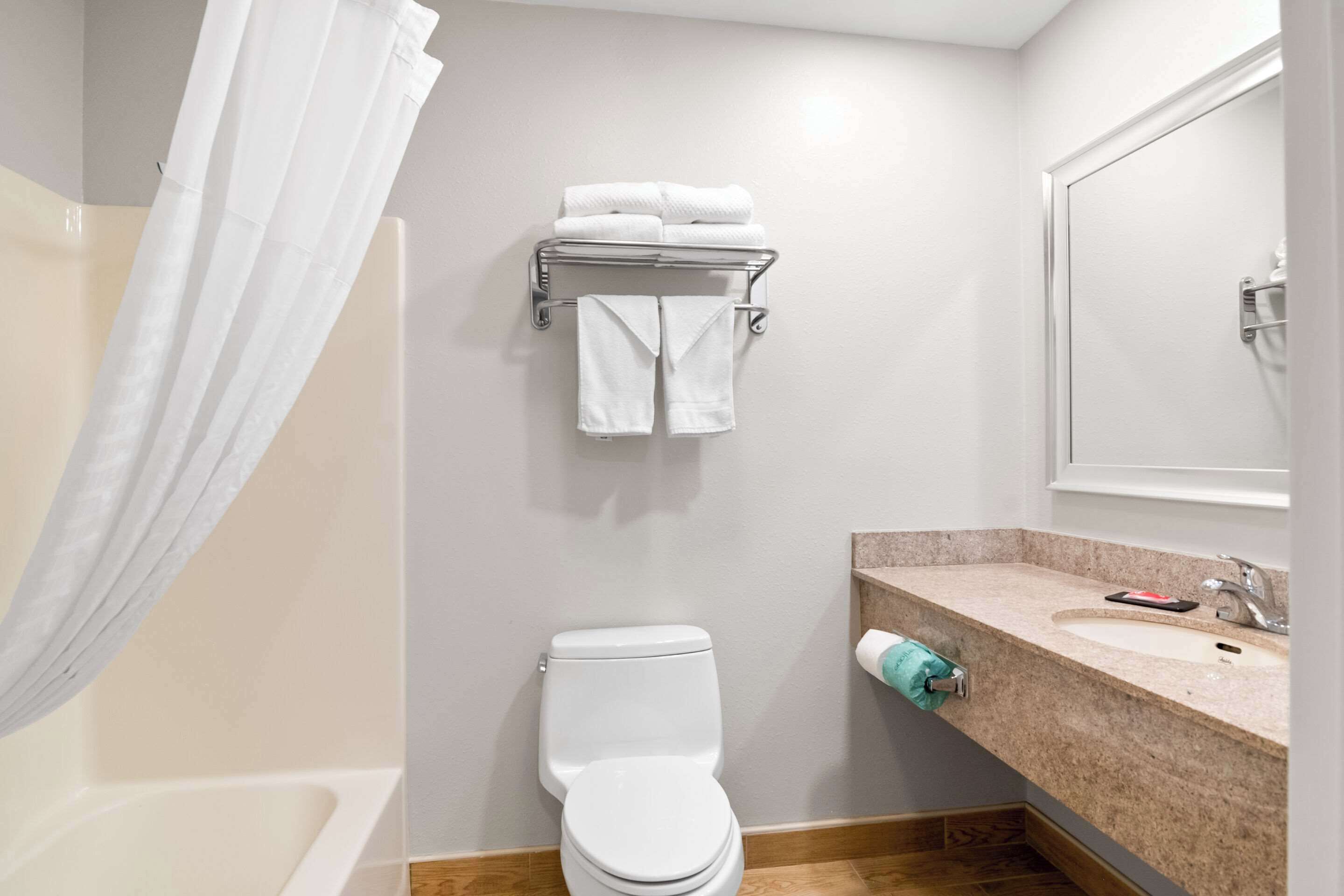A bathroom with a toilet, a sink, a towel rack with folded towels, and a shower curtain.