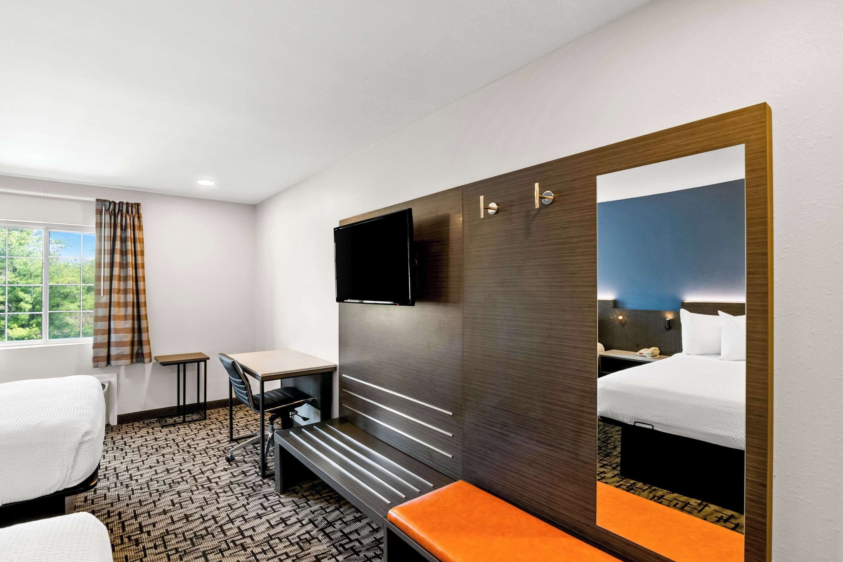 A hotel room with a bed, a desk, a chair, a bench, a television, and a window with curtains.