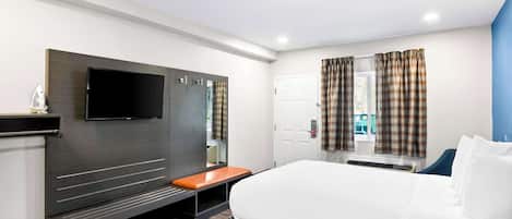 A hotel room with a bed, a TV mounted on the wall, a bench, and a window with curtains.