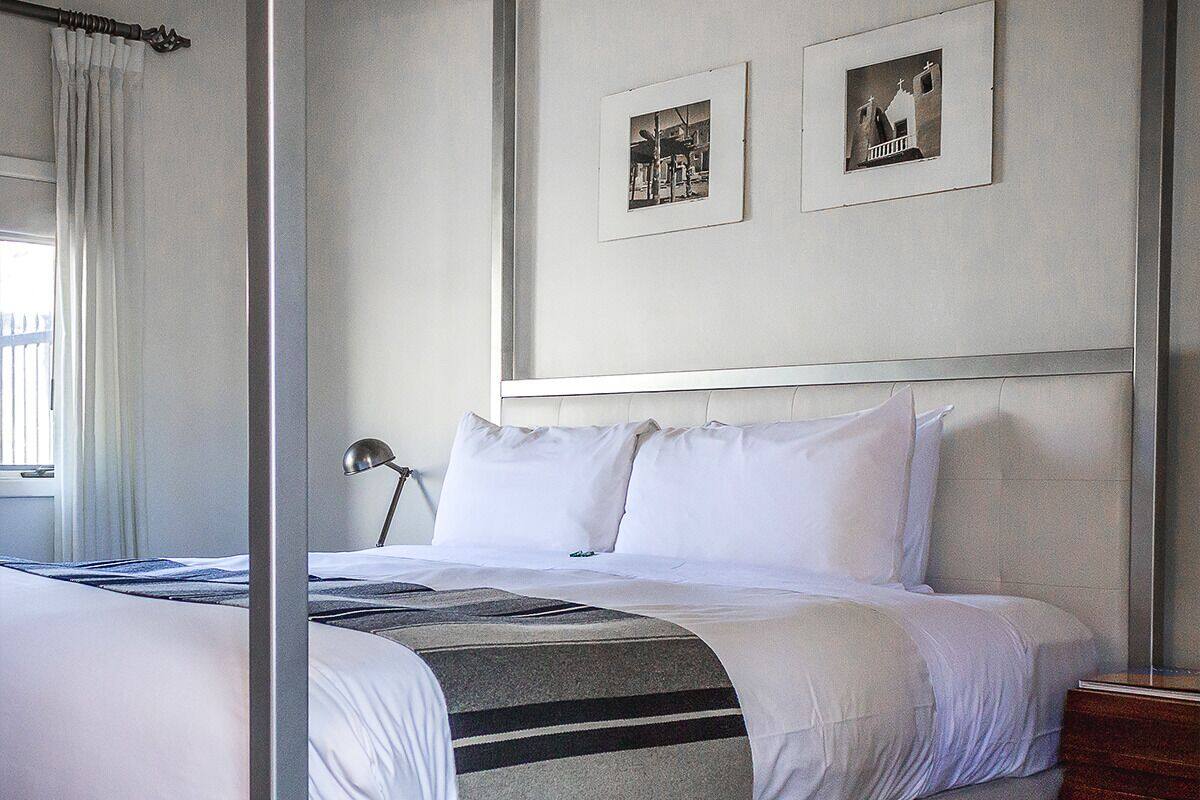 A four-poster bed with white linens, a grey and black striped throw blanket, and two framed pictures on the wall.
