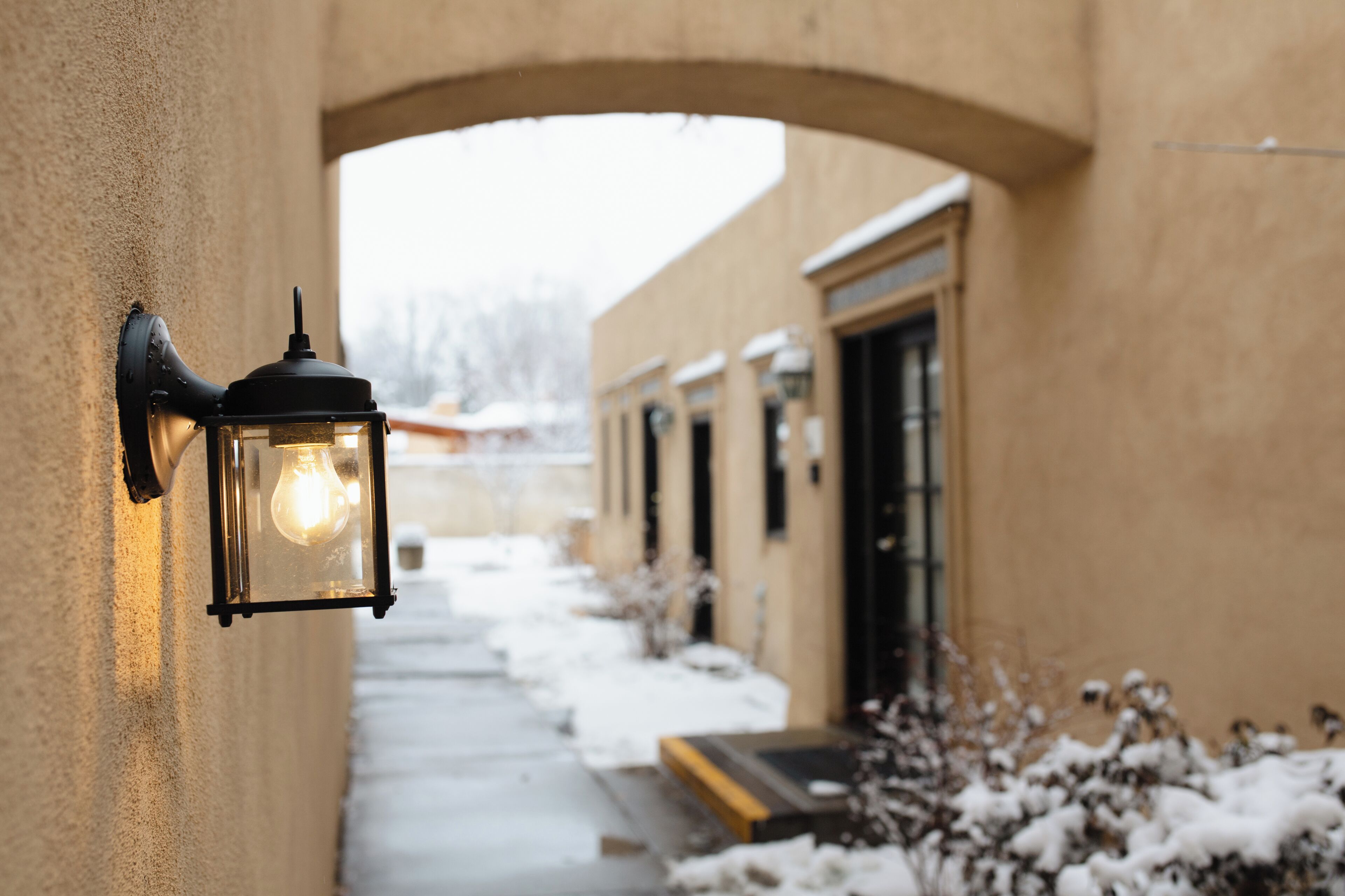 A corridor with a wall-mounted light fixture, a door, and snow on the ground.