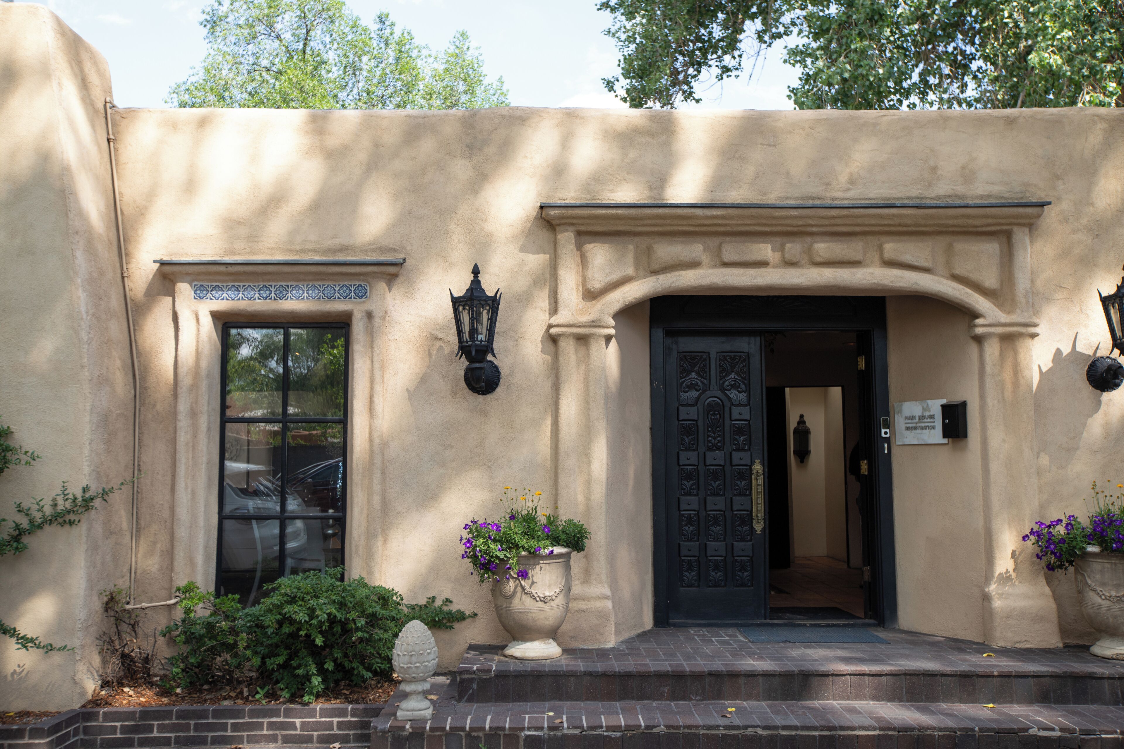 A building facade with a black door, a window, and two wall-mounted light fixtures.