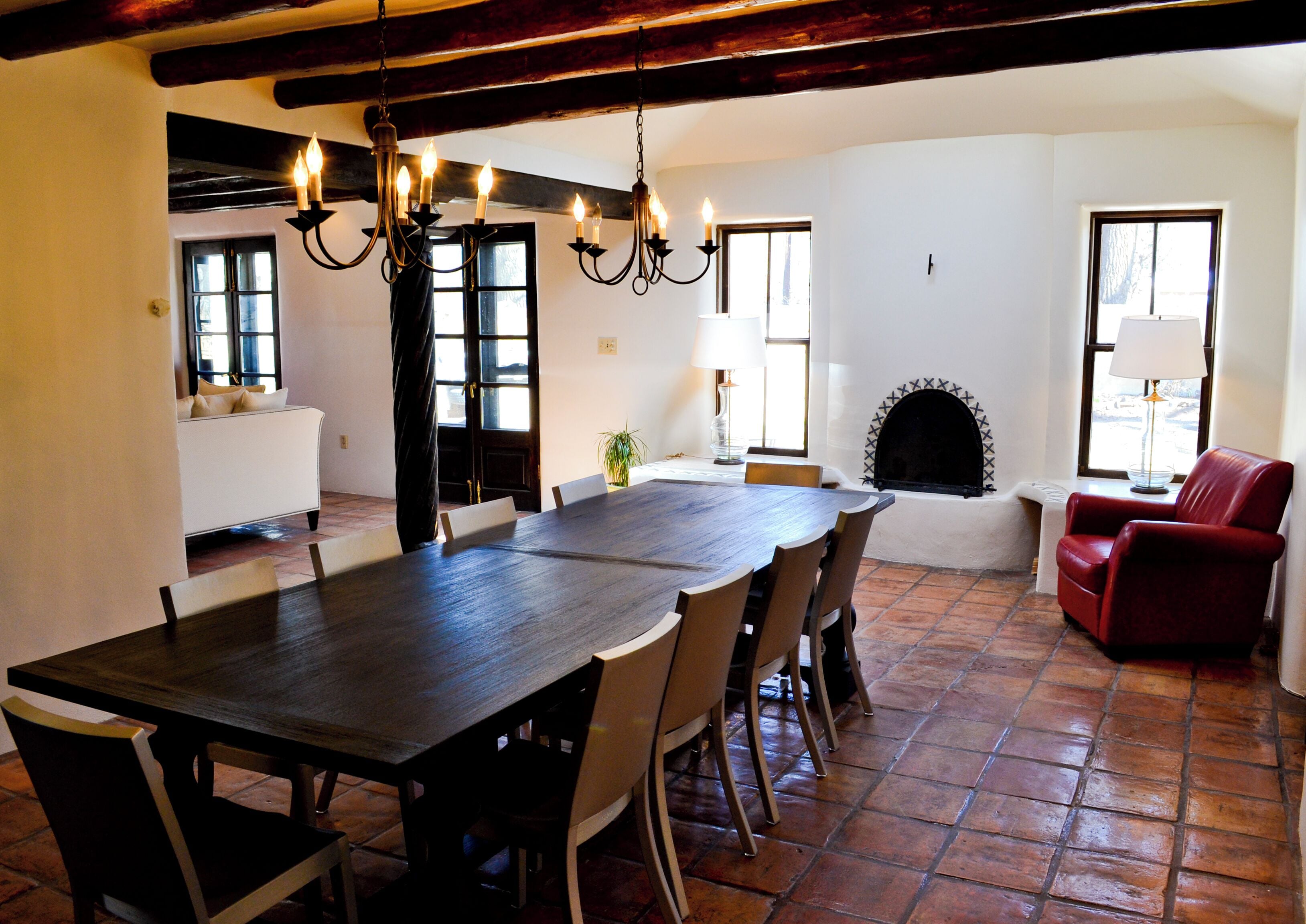 A dining area with a large wooden table, multiple chairs, a chandelier, a fireplace, and a red armchair.