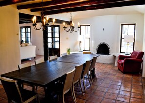 A dining area with a large wooden table, multiple chairs, a chandelier, a fireplace, and a red armchair. - Palacio De Marquesa (Taos)
