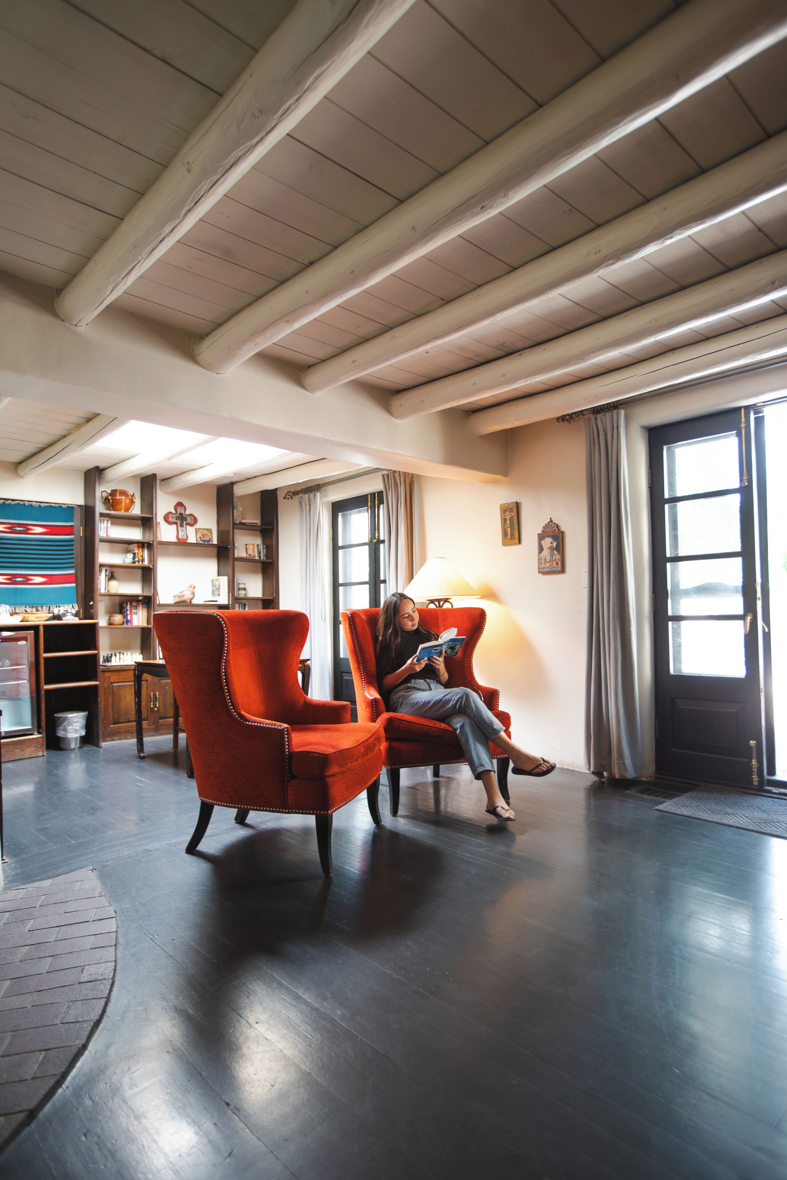 Una habitación espaciosa con techo alto, vigas de madera, un ventanal con cortinas y un sillón rojo.