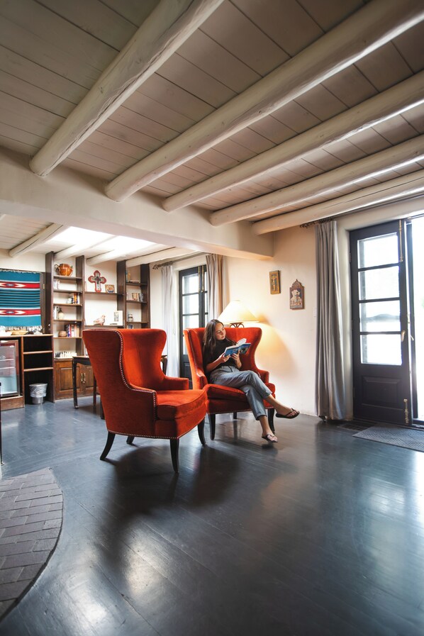 A spacious room with a high ceiling, wooden beams, a large window with curtains, and a red armchair.