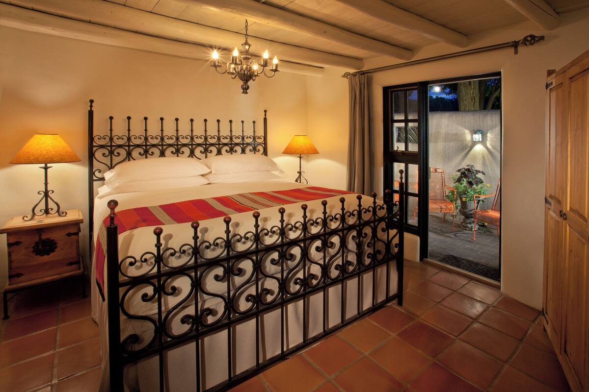 A bedroom with a wrought iron bed frame, two bedside tables with lamps, a chandelier, and a view of the outside through a sliding glass door.