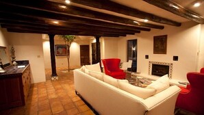 A cozy living room with a white sofa, red chairs, a fireplace, and exposed wooden beams.