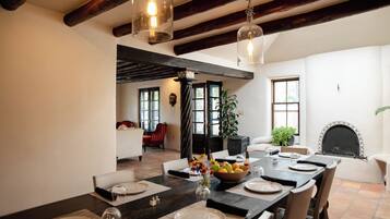 A dining area with a long table set for six, a fireplace, and a view of the living room.