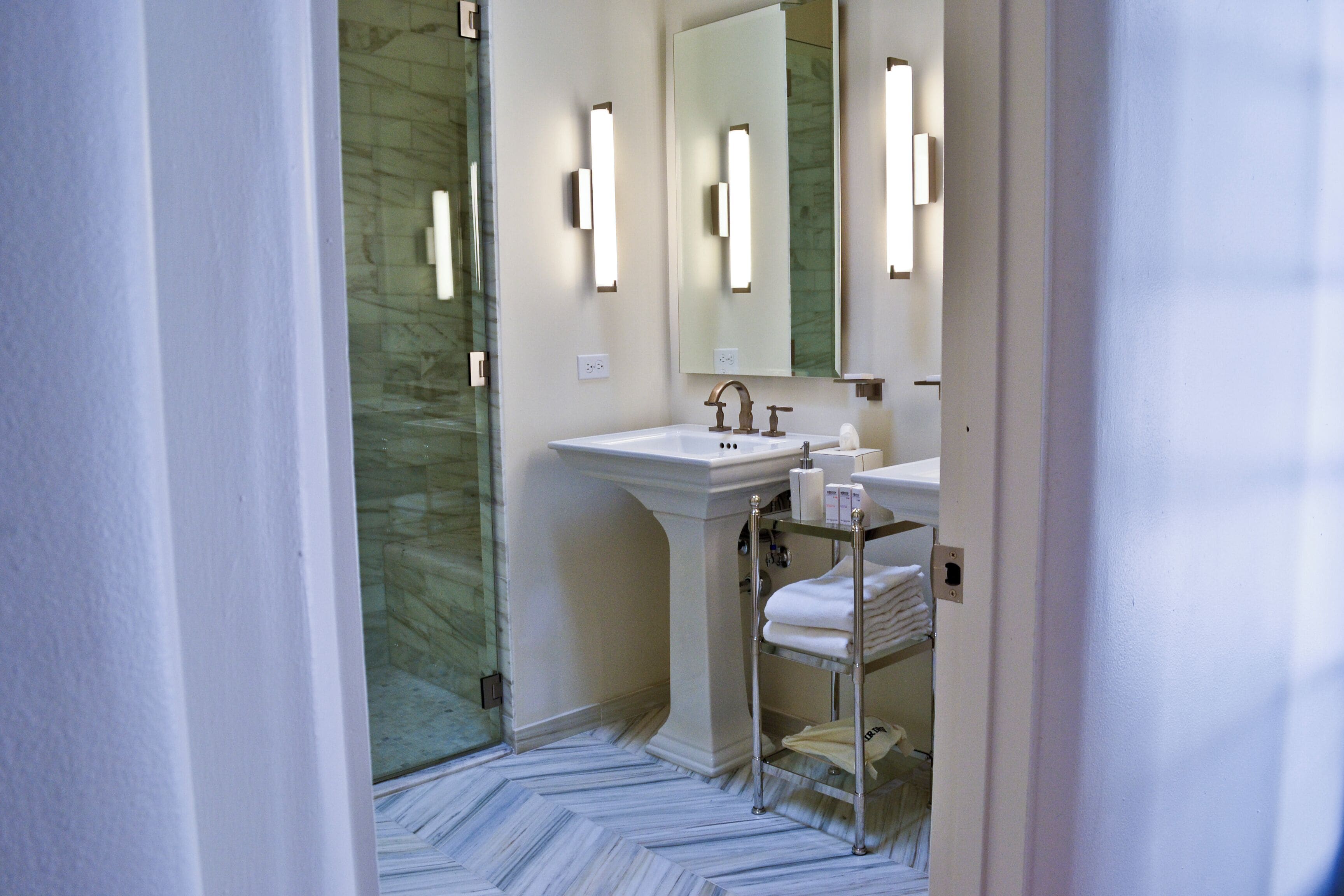 A bathroom with a marble floor, a sink with a mirror, and a towel rack.