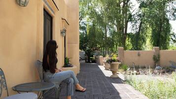 A woman seated on a metal chair outside a building with a tiled wall and a door.