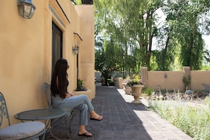 A woman seated on a metal chair outside a building with a tiled wall and a door.