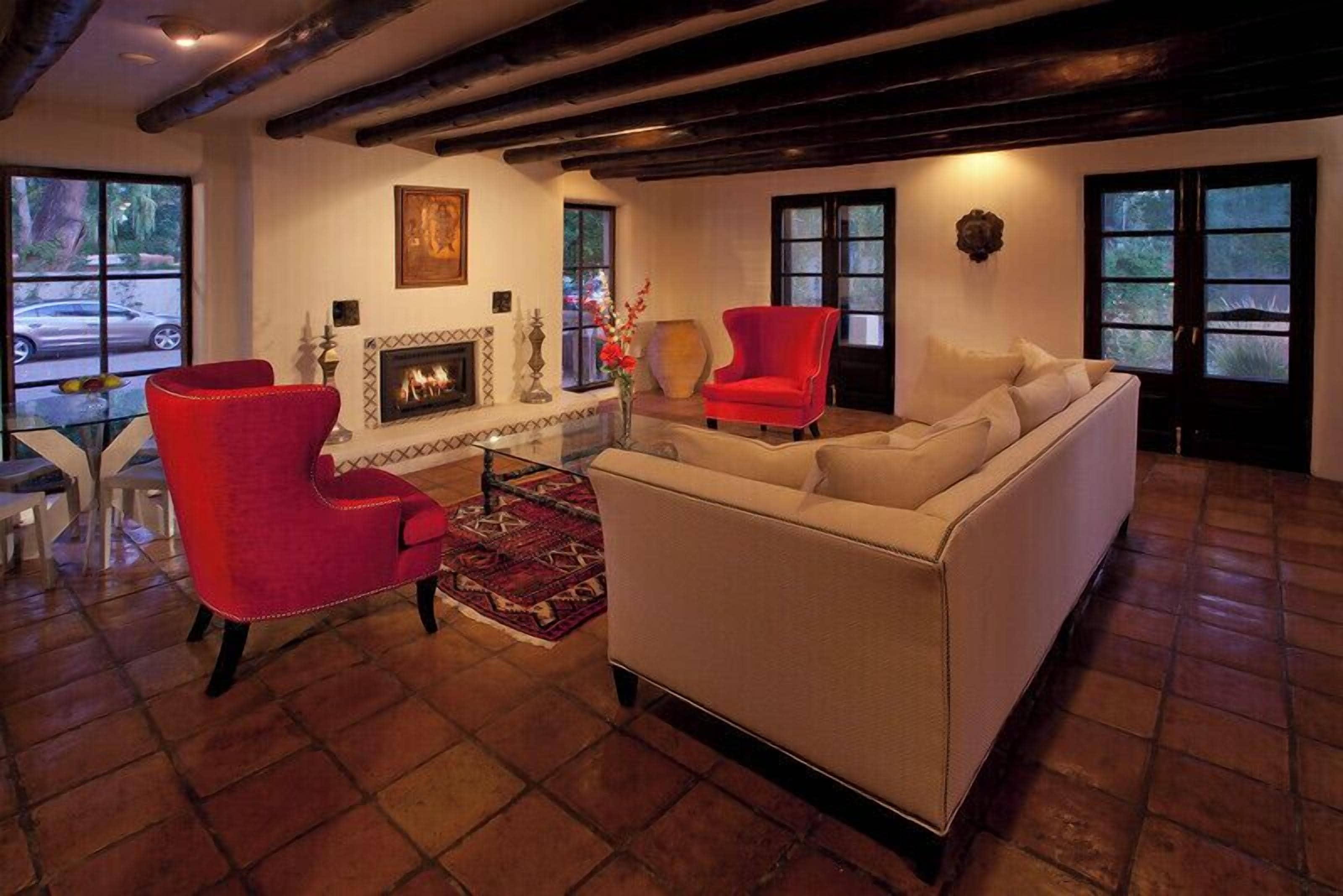 A living room with a fireplace, red chairs, a beige sofa, and a tiled floor.