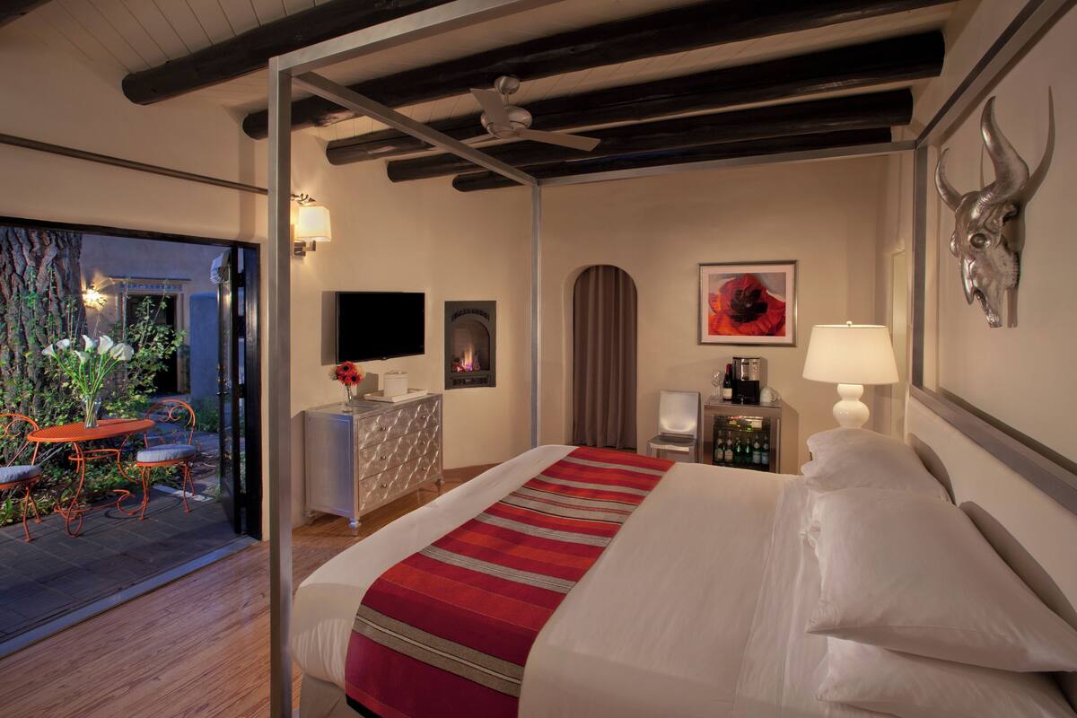 A hotel room with a large bed, a desk with a computer, a chair, a TV, and a window with a view of a garden.
