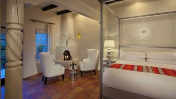 A hotel room with a bed, a fireplace, two chairs, a table with a bottle, and a window.