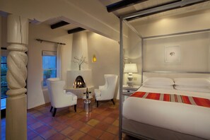 A hotel room with a bed, a fireplace, two chairs, a table with a bottle, and a window. - Palacio De Marquesa (Taos)