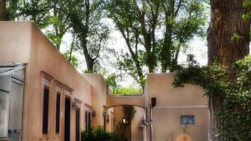 A rustic outdoor area with a large copper pot, surrounded by pebbles, in front of a building with a beige facade and multiple windows.