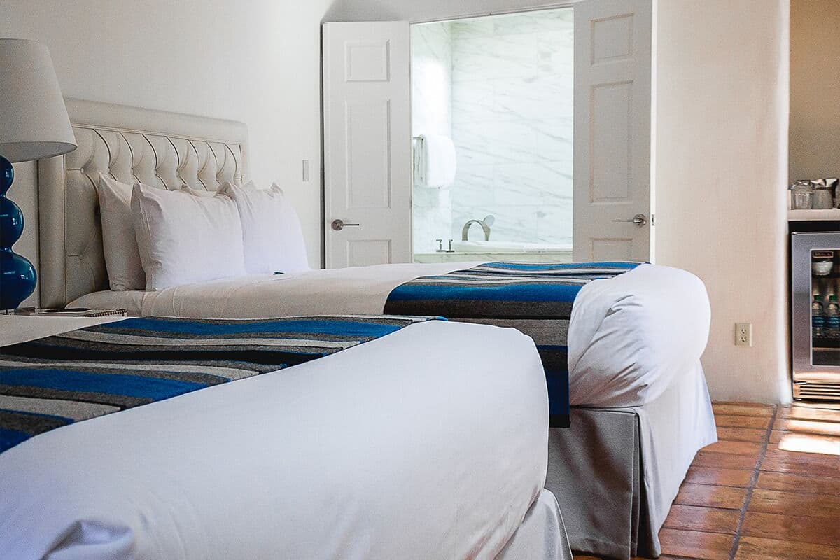 A hotel room with two beds, a large window, a bathroom, and a kitchenette.