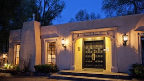 A building with a black door, two lit wall sconces, and a small sign above the door.