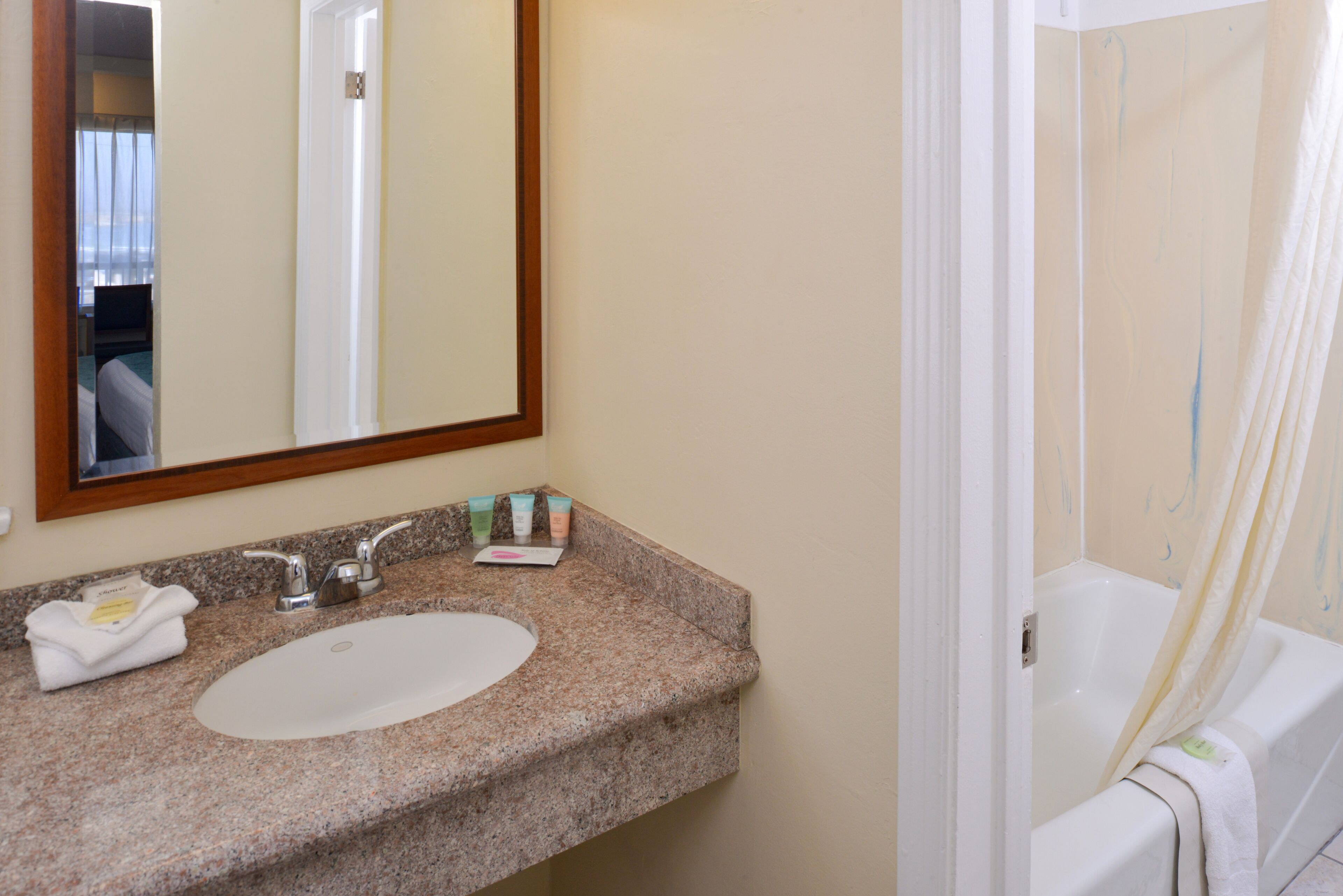 A bathroom with a granite countertop, a white sink, a mirror, and a bathtub.