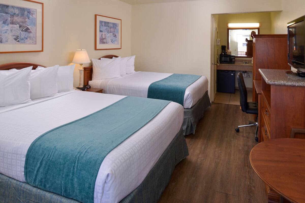 A hotel room with two beds, a desk, a chair, a television, and a kitchenette.