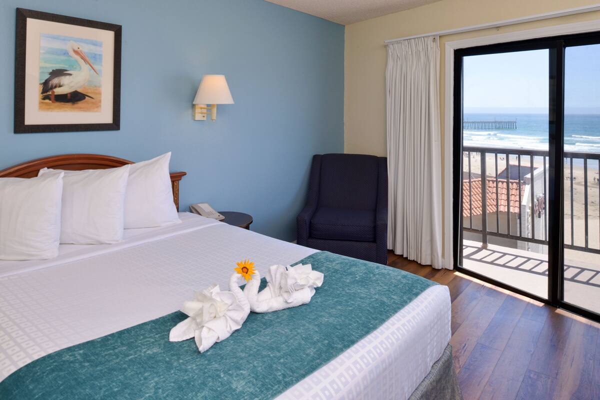 A hotel room with a bed, a chair, a painting, and a view of the ocean.
