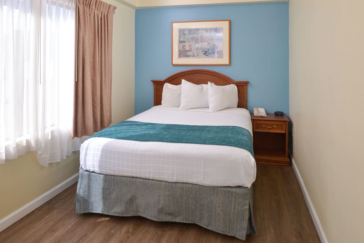 A neatly made bed with a wooden headboard, a bedside table with a telephone, and a framed picture on the wall.