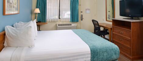 A hotel room with a bed, a desk, a chair, a television, and a window with curtains.