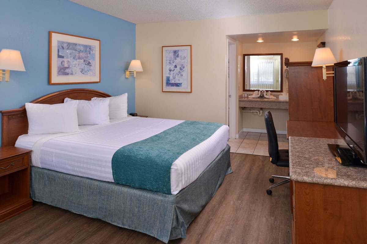 A hotel room with a bed, a desk, a chair, a television, and a bathroom visible through an open door.