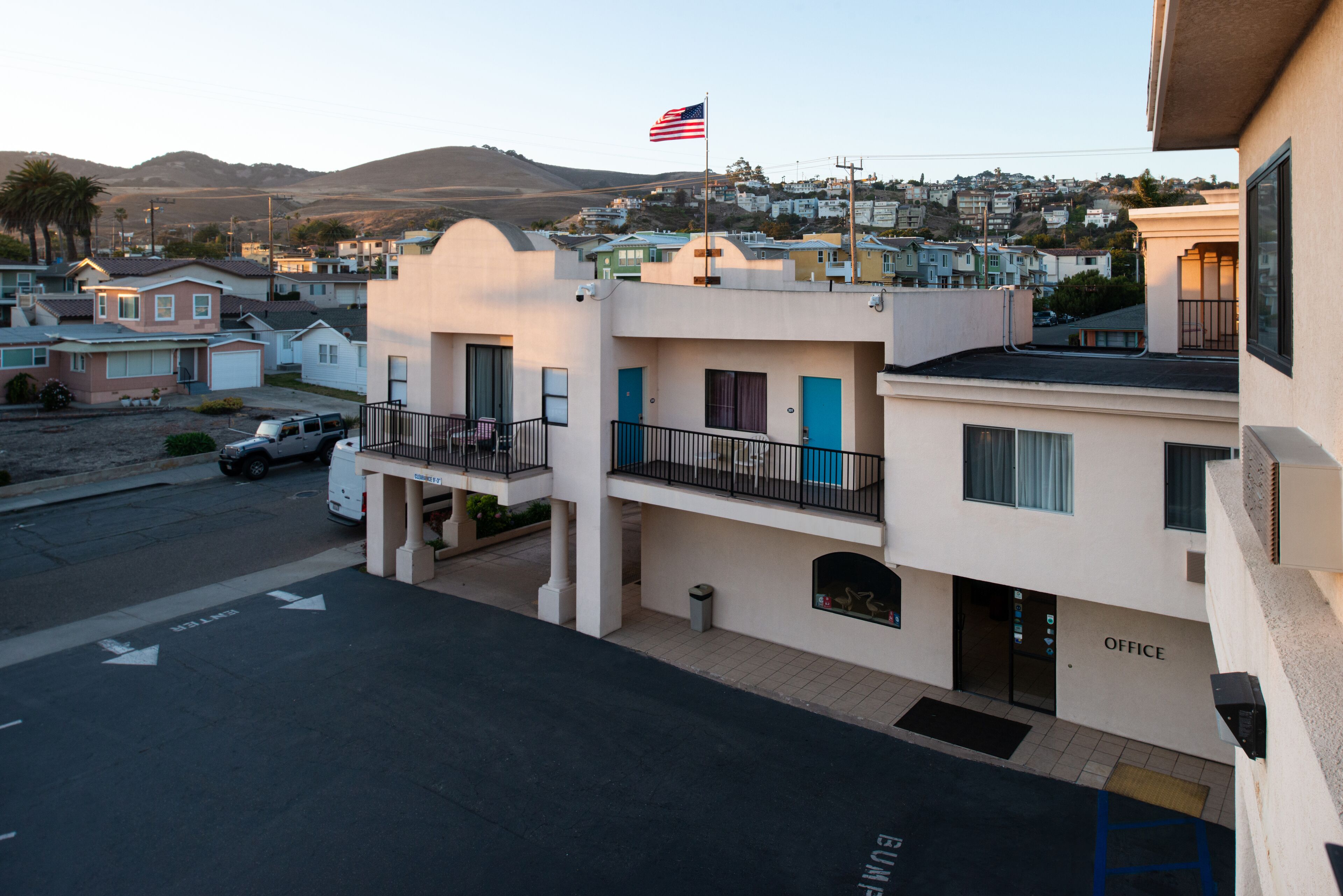 A multi-story building with a flag, a parking lot, and a street view.