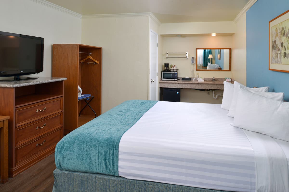 A hotel room with a bed, a TV, a desk with a microwave, and a bathroom with a sink and mirror.