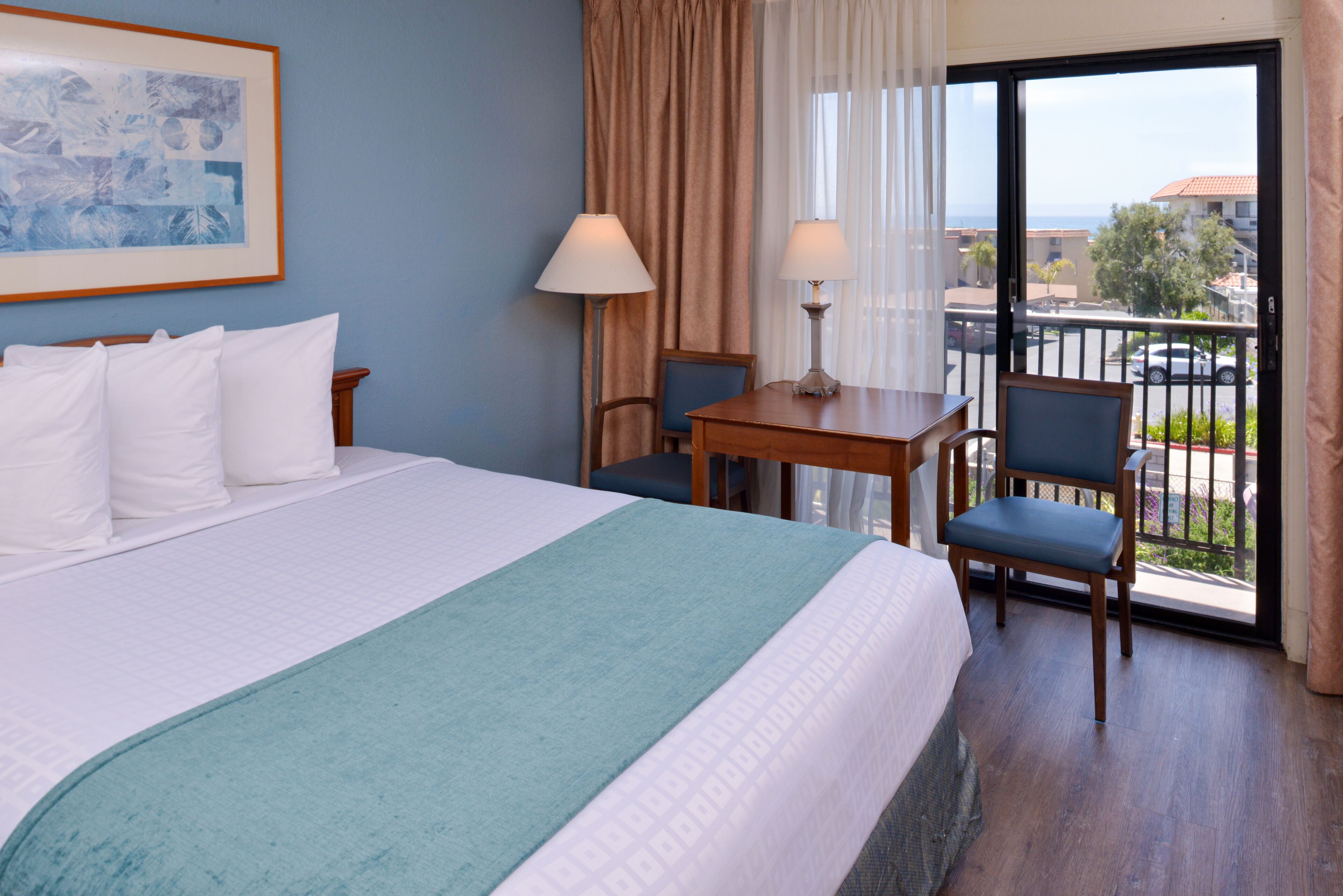 A hotel room with a bed, a desk, a chair, and a view of the outside.