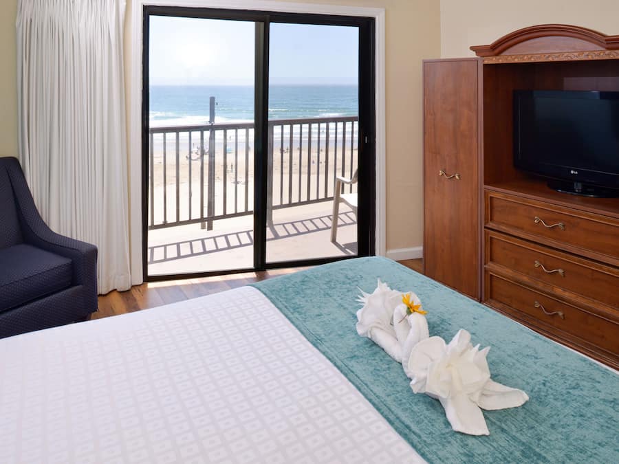 A hotel room with a bed, a TV, a balcony with a view of the beach, and a chair.