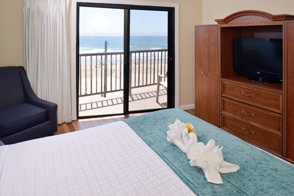 Habitación de hotel con cama, televisor, balcón y vista a la playa, además de una silla.