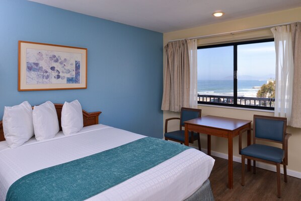 Habitación de hotel con una cama, un escritorio y una silla. Se ve el océano desde la ventana.