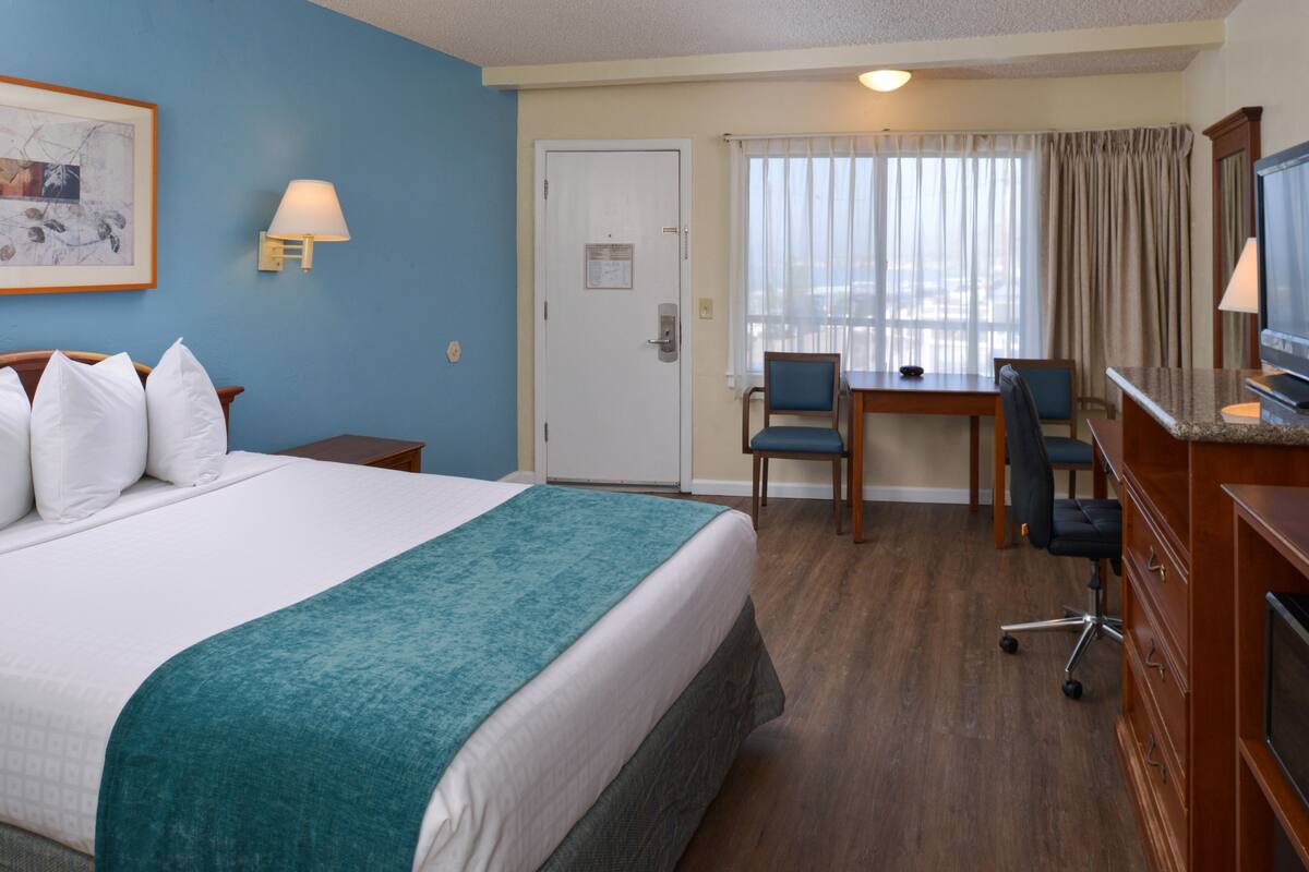 A hotel room with a large bed, a desk, a chair, a TV, and a window with curtains.