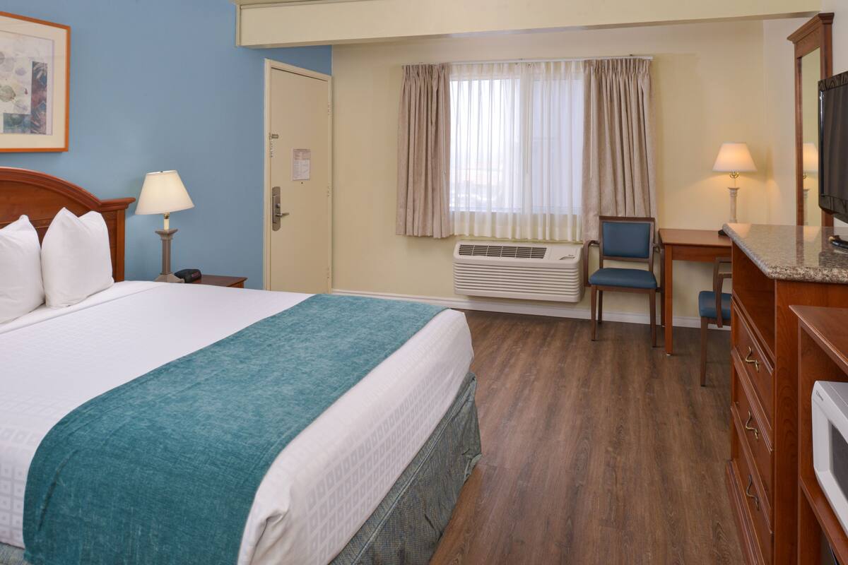 A hotel room with a large bed, a desk, a chair, a television, and an air conditioning unit.