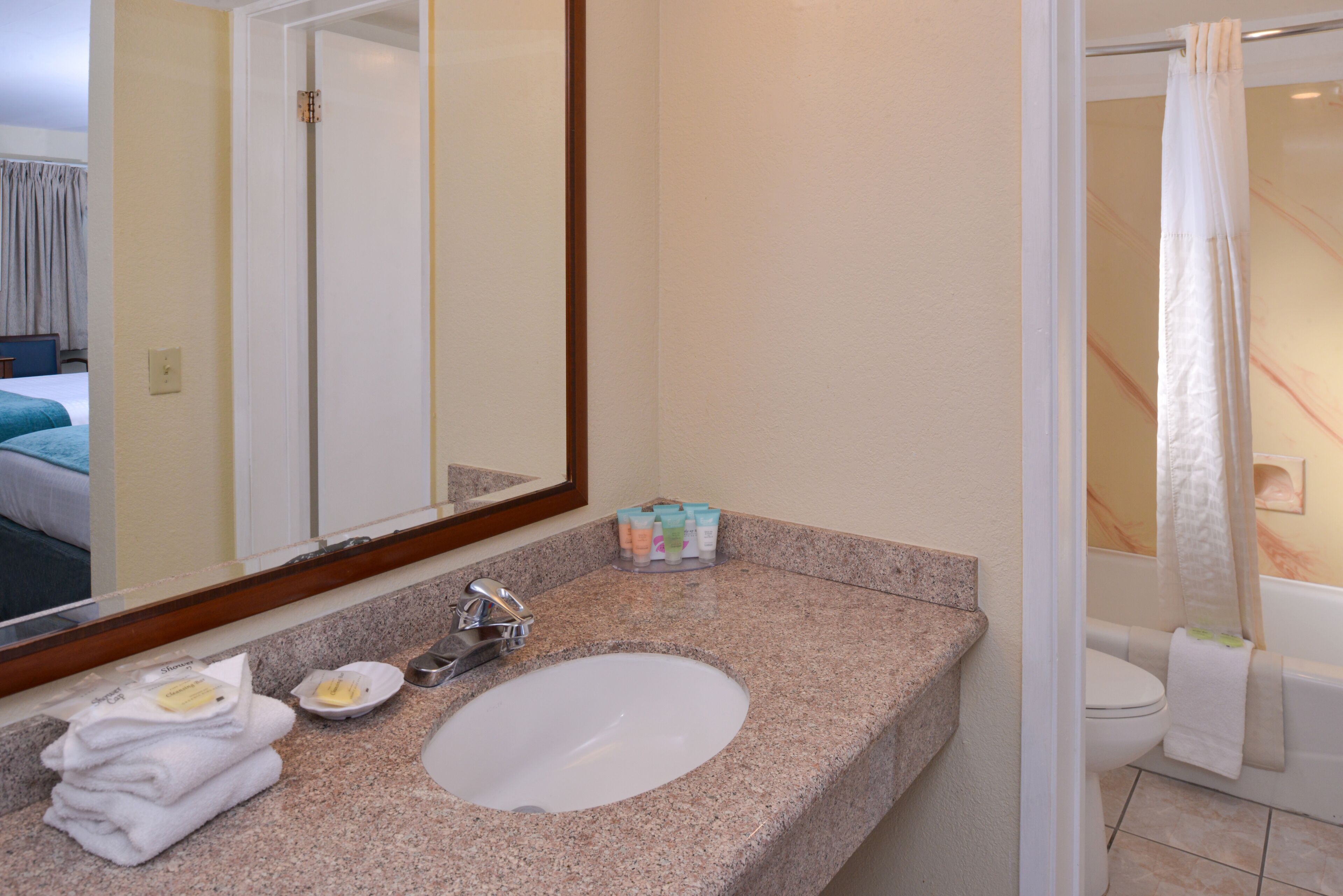 A bathroom with a granite countertop, a sink, a mirror, a toilet, and a shower curtain.