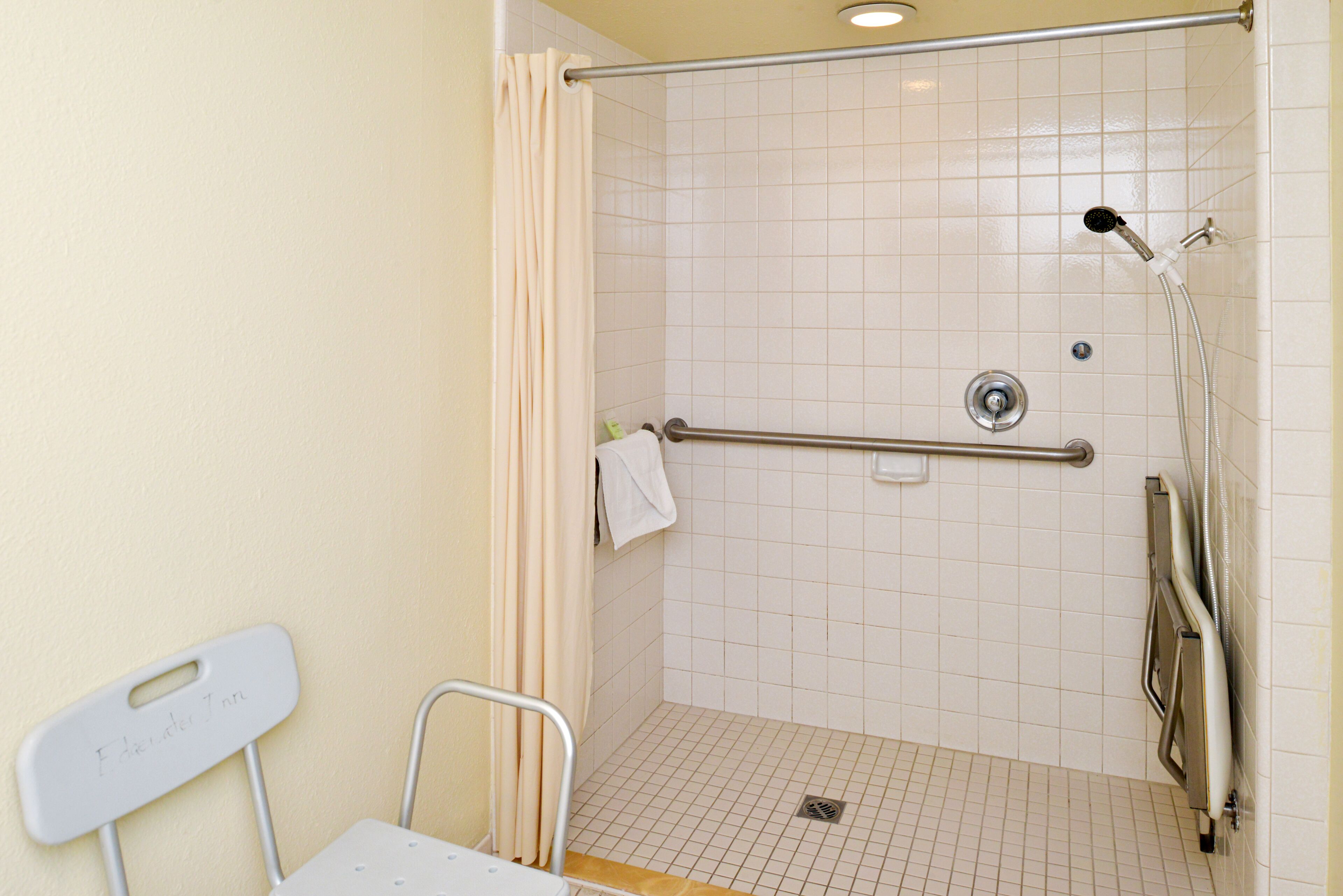 A shower area with a grab bar, a white chair, and a towel rack.