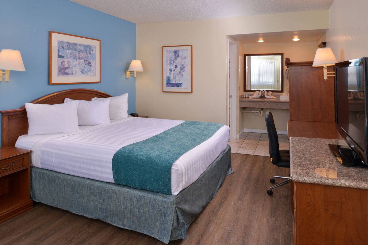 A hotel room with a bed, a desk, a chair, a TV, and two framed pictures on the wall.