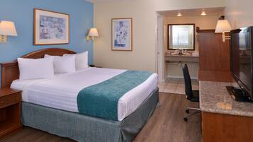 A hotel room with a bed, a desk, a chair, a TV, and two framed pictures on the wall.