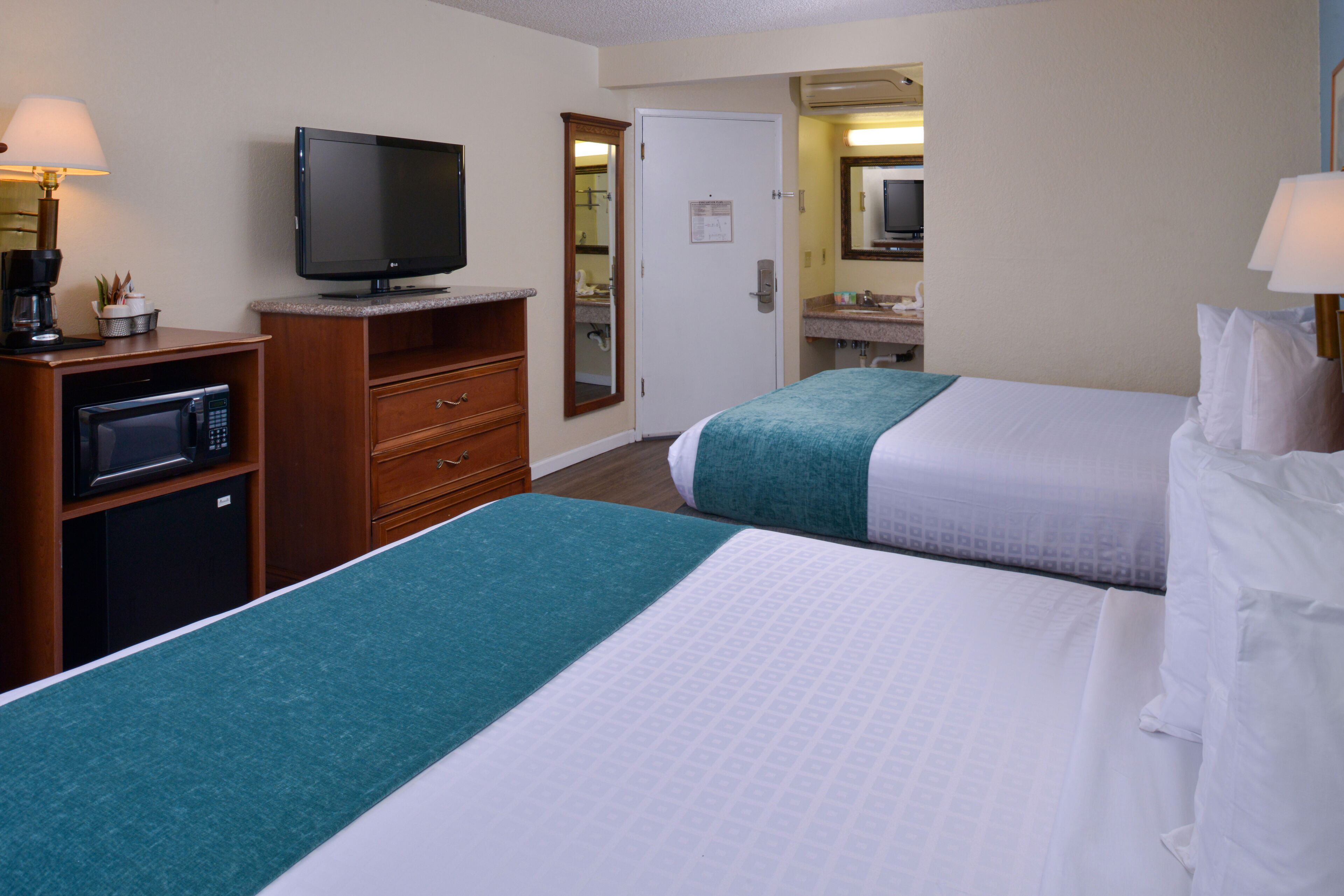 A hotel room with two beds, a television, a microwave, and a small kitchenette.