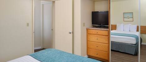 A hotel room with a bed, a television on a dresser, a mirror, and a door leading to another room.