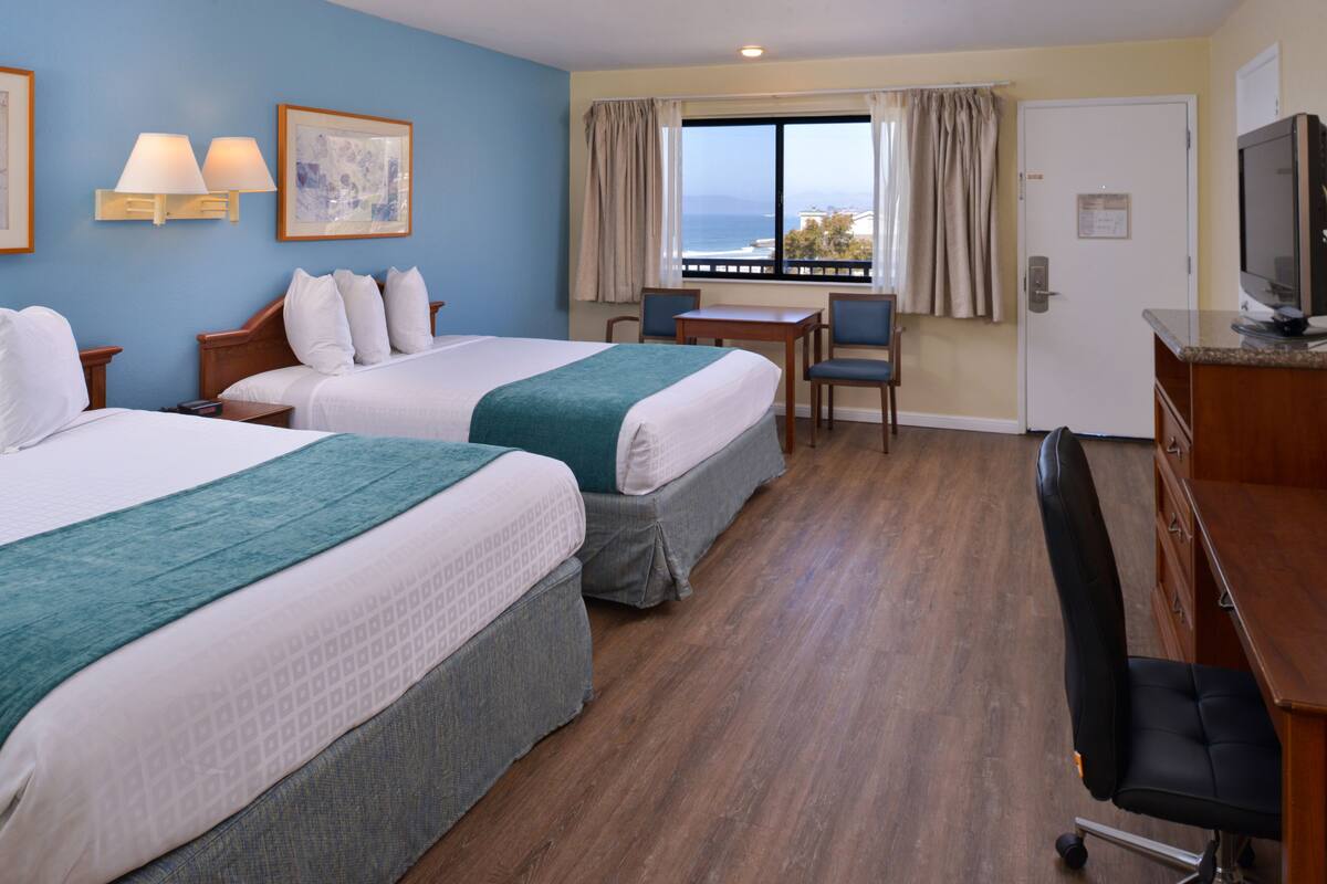 A hotel room with two beds, a desk, a chair, and a television.