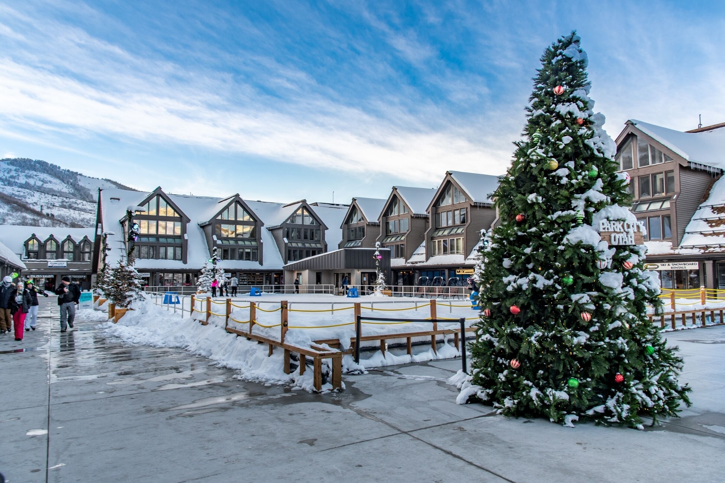 Una plaza nevada con un gran árbol de Navidad y edificios tradicionales.