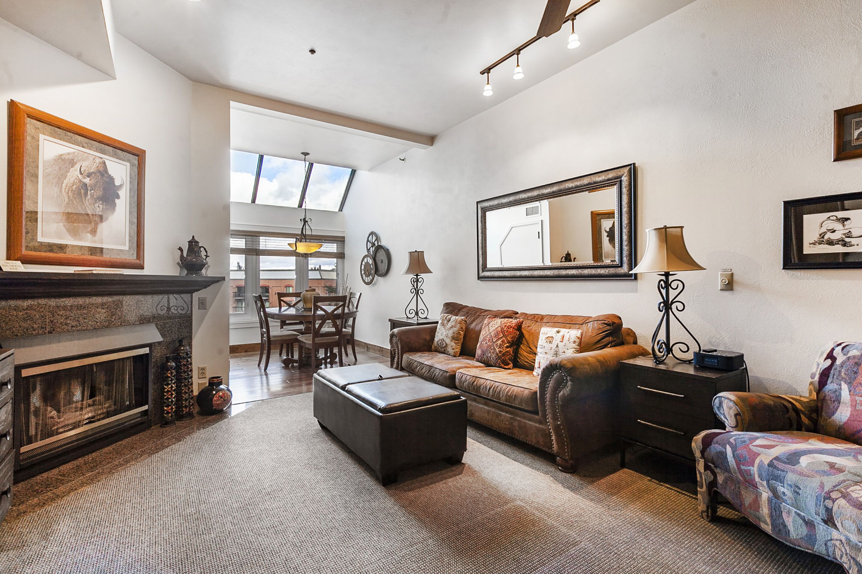 A living room with a fireplace, a sofa, a patterned armchair, and a dining area with a table and chairs.