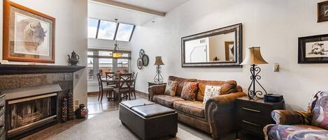A living room with a fireplace, a sofa, a patterned armchair, and a dining area with a table and chairs.