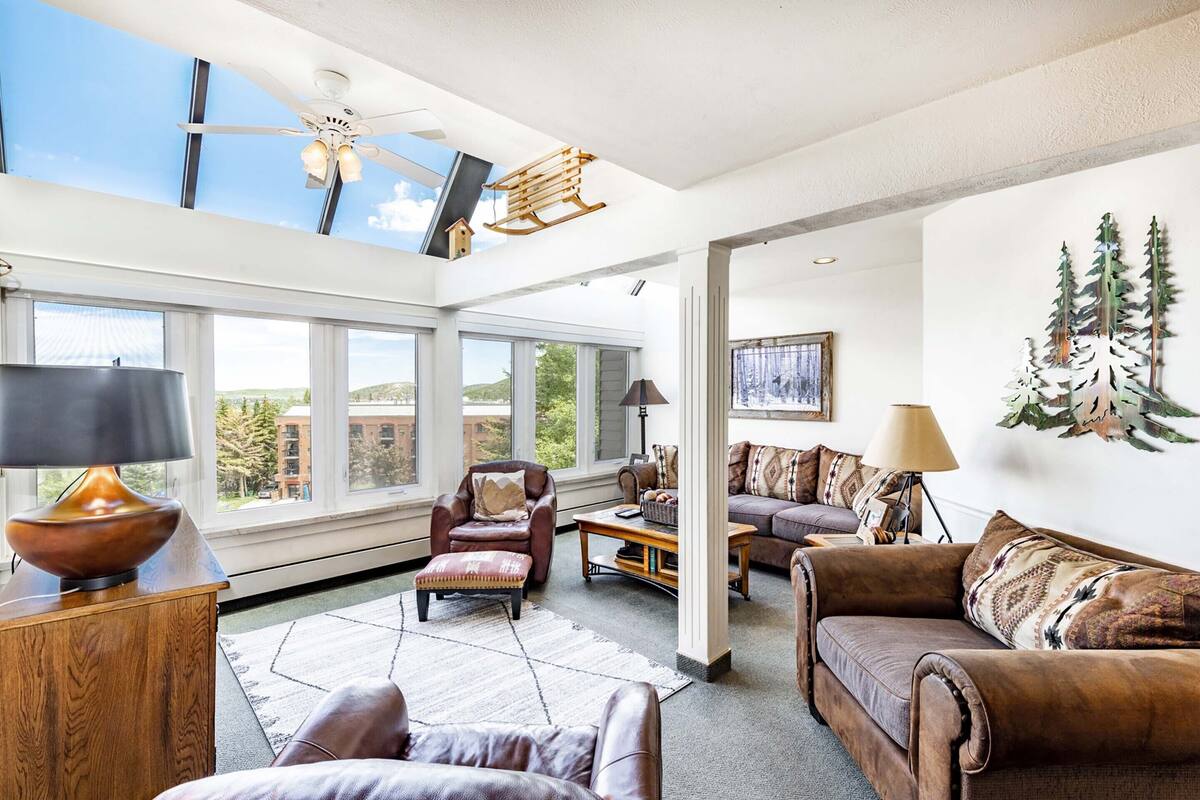 Un salon spacieux doté de grandes fenêtres, d’un ventilateur de plafond et d’une cheminée.